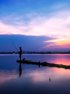 Photo by Pixabay A serene silhouette of a fisherman on a jetty during a vivid sunset over placid waters.
